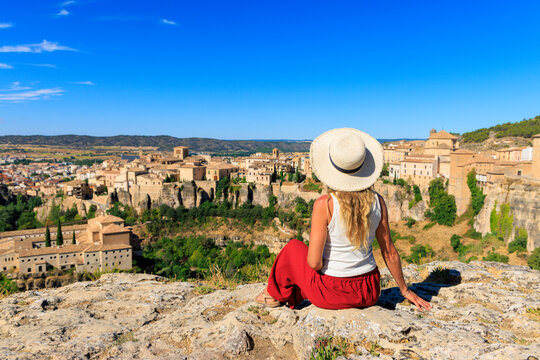Young woman tourist sitting on cliff enjoying panoramic view of Cuenca, tour tourism in Spain