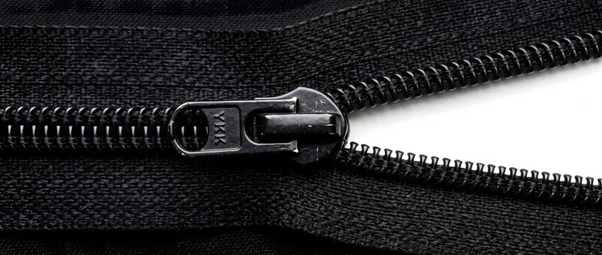 Close up view of black metal zipper slide on textured dark fabric tape.