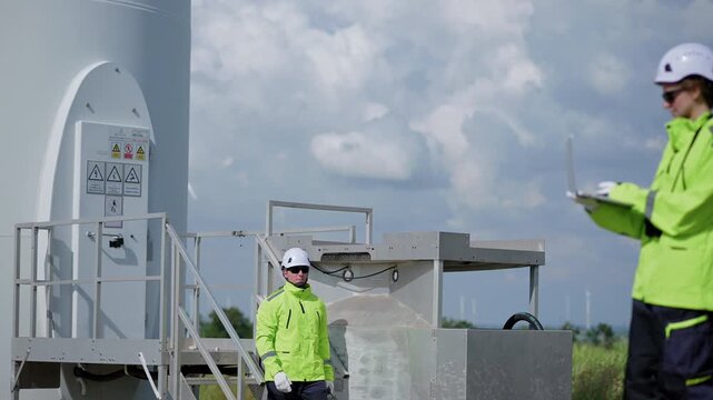 Engineers wearing safety helmets and jackets inspecting a wind turbine at wind farm at sunset. Concept renewable energy, sustainable technology wind power maintenance and environmental engineering.