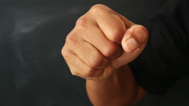 A close up view of a human hand clenched into a tight fist against a dark background.