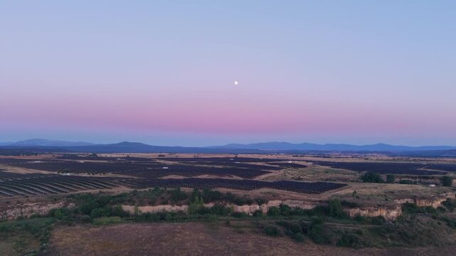 Aerial view of a large solar farm at dusk with the moon visible in the sky over the landscape in Ciudad Rodrigo, Castile and Leon, Spain.