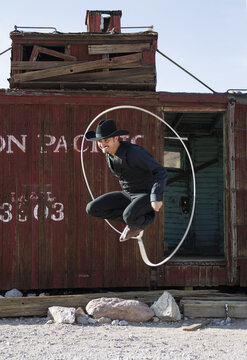 Rhyolite, Nevada, United States - 27 March 2011: View of a man in a cowboy hat jumping through a lasso in front of a weathered red train car in Rhyolite.