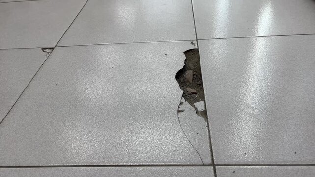 Broken ceramic floor tile with cracks and deep hole inside room