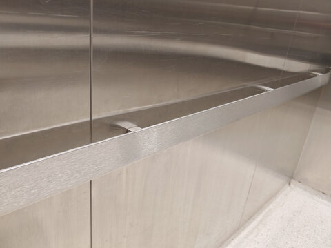 a brushed stainless steel handrail and wall panels inside a commercial elevator cabin, targeting modern architecture and building interior concepts.