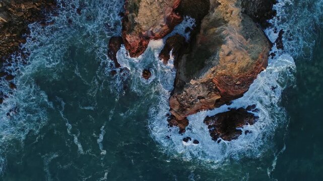 Aerial view of rocky cliffs meeting the crashing waves of the Atlantic Ocean in Portugal.