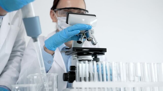 Scientists in personal protective equipment conducting medical biology research, collaborating on experiments and analyzing samples under a microscope in a modern laboratory for discovery