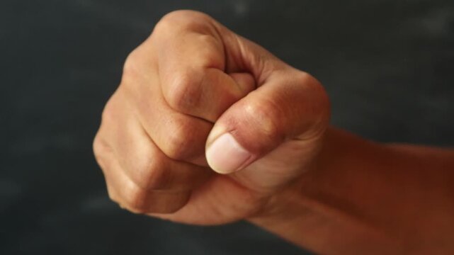 Close up of a human hand clenched into a tight fist against a dark background.