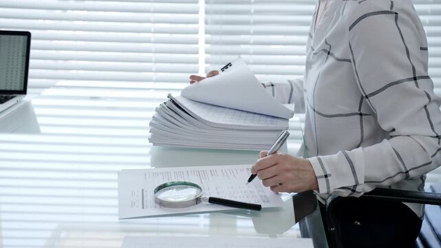 Professional woman categorizing important business documents and financial statements on an office desk. Managing a stack of files during a detailed audit
