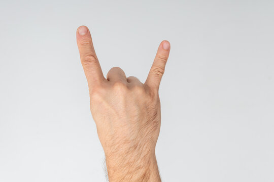 Male hand making the rock and roll devil horns gesture, symbolizing heavy metal music, energy, excitement and rebellious attitude with fingers extended against white background