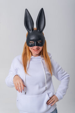 Woman with red hair wearing a dark rabbit mask and a white sweatshirt for a playful and intriguing look, portraying concepts of disguise, anonymity, and Easter celebrations