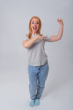 Young woman with a surprised expression proudly flexing her bicep and pointing at it, symbolizing power, success, achievement, and female empowerment in everyday life
