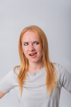 Young redhead woman showing skepticism and uncertainty, scrunching her nose and narrowing her eyes while looking to the side with a doubtful, annoyed expression on a white background