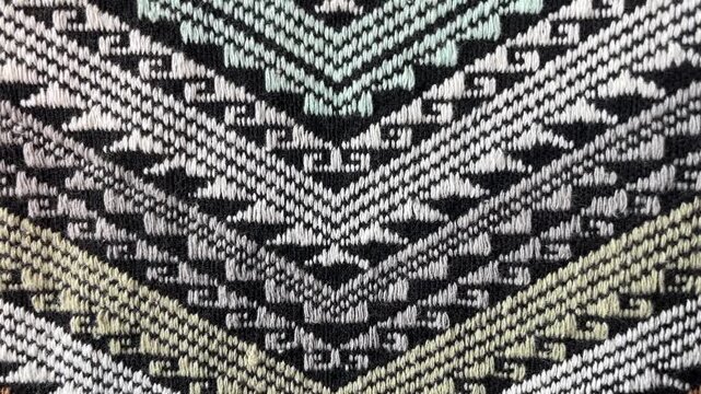 Tribal Textile Pattern: An intricate, geometric pattern woven into a fabric, featuring sharp angles, zig-zag lines, and a blend of black, white, and muted green hues.