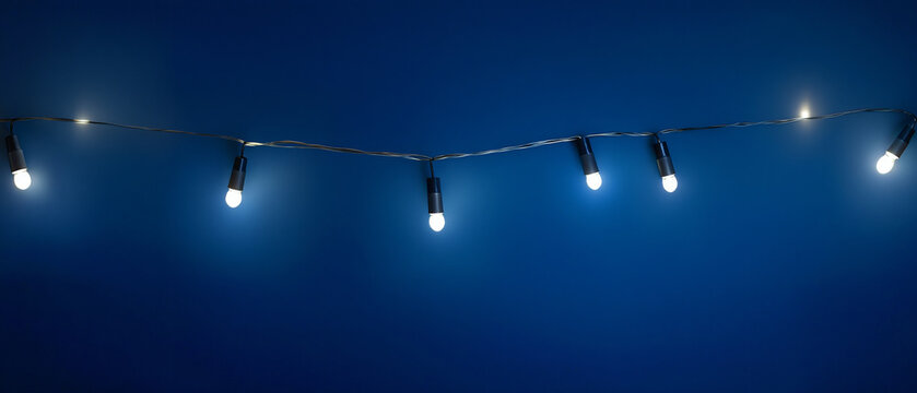 String of glowing vintage Edison style light bulbs hanging against a solid deep blue background