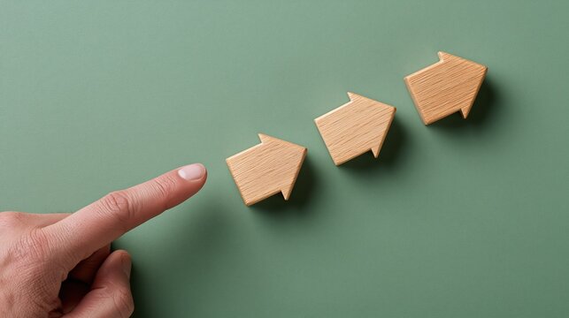 Finger pointing towards three wooden arrow shapes symbolizing progress and direction on a green background