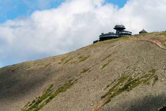 Karpacz, Poland - 28 July 2026: View of the Snezka mountain summit with its distinctive disc-shaped observatory building, set against a rocky slope under a cloudy blue sky.
