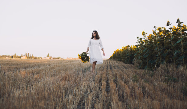woman in a white dress holding a bouquet of wild flowers with sunflowers in a field