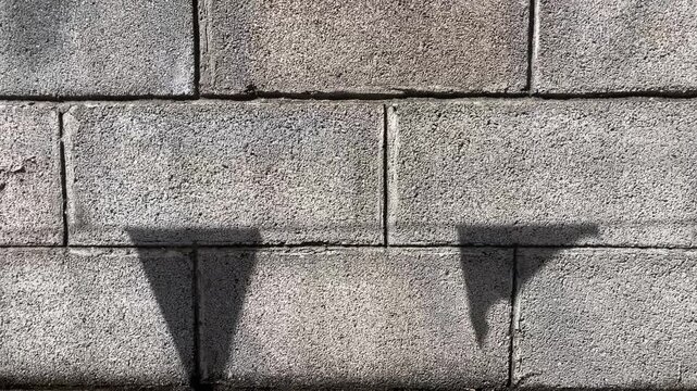 Stone Wall Texture with Shadow: Close-up view of a grey stone wall with distinct shadows cast by an unseen object, highlighting the rough texture and geometric pattern of the construction.