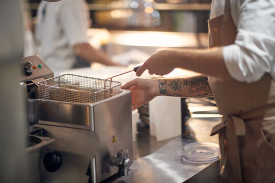close up of fryer and chef hand . Cook in Professional Modern  kitchen, restaurant concept