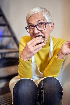 senior woman taking a break eating cupcake after making them in confectionery shop