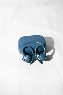 Pair of blue true wireless sports earbuds leaning against a closed blue charging case on a white fabric background