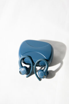 Pair of blue true wireless sports earbuds leaning against a closed blue charging case on a white fabric background