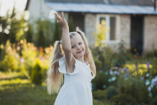 a cute five-year-old girl in a white dress is playing in a green summer garden. happy childhood