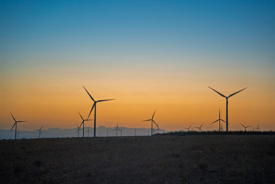 Wind turbines silhouetted against a colorful sunset sky, generating clean renewable energy on a vast wind farm