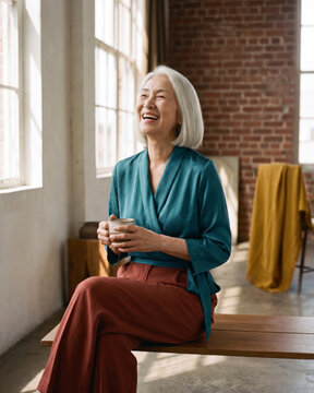 Playful mature woman laughing on wooden bench in industrial loft with warm natural light