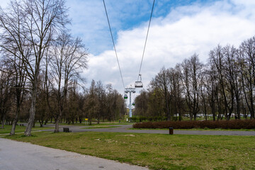 Cable car ride over a tranquil park landscape with tall bare trees and green grass under a partly cloudy spring sky © MAKSYM