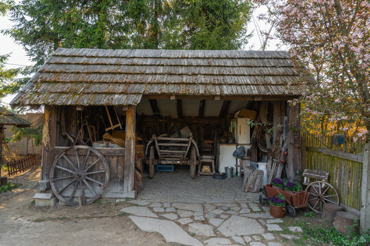 Rustic wooden shed with old farm wagon, wooden wheels, and antique tools stored inside in a peaceful rural country setting