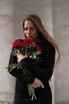 Fragrant peonies held by young woman in black dress during outdoor portrait session with copy space
