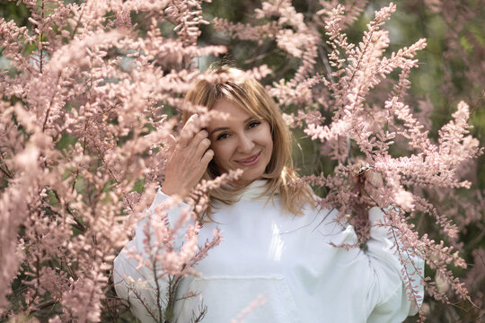 Woman blossoms spring enjoying nature surrounded by pink tamarisk flowers in sunlight