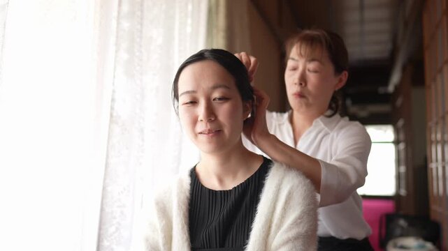 A woman in a white cardigan sits by a window while a hairstylist adjusts her hair from behind. Japan, April 19, 2025, spring.