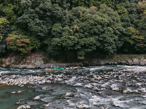 Kyoto, Kyoto, Japan - 28 August 2026: View of a traditional wooden boat with passengers navigating the rocky Hozugawa River, framed by dense green forest in Kyoto, Kyoto, Japan.