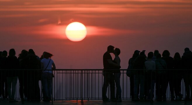Silhouettes of people watching and a romantic couple kissing during a spectacular total solar eclipse at sunset, seen from the Eiffel Tower observation deck in Paris.