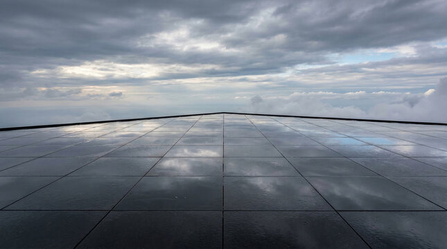 Dramatic cloudy sky reflected on a glossy tiled rooftop terrace.