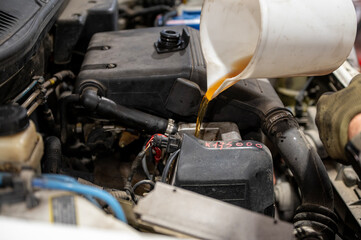 Fototapeta premium Mechanic pouring engine oil into a car engine during routine maintenance in an automotive workshop, close-up of the engine compartment.