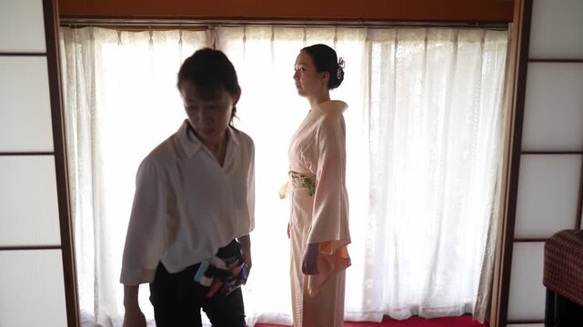 A woman stands by a bright window wearing a peach kimono underlayer secured at the waist. Japan, April 19, 2025, spring.