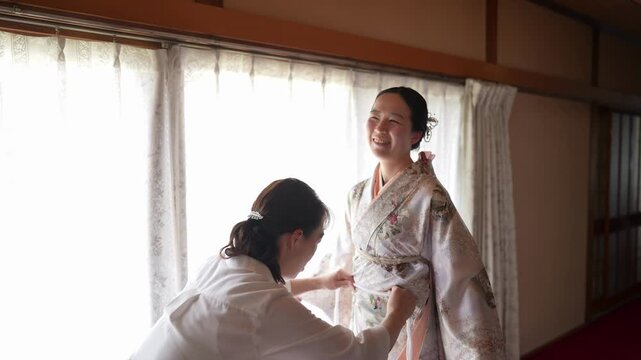 A woman looks to the side as an assistant adjusts the front of her patterned kimono. Japan, April 19, 2025, spring.