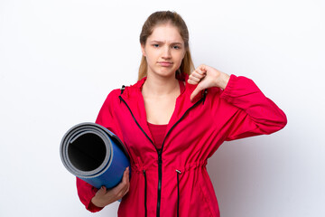 Teenager girl going to yoga classes while holding a mat isolated on white bakcground showing thumb down with negative expression © luismolinero