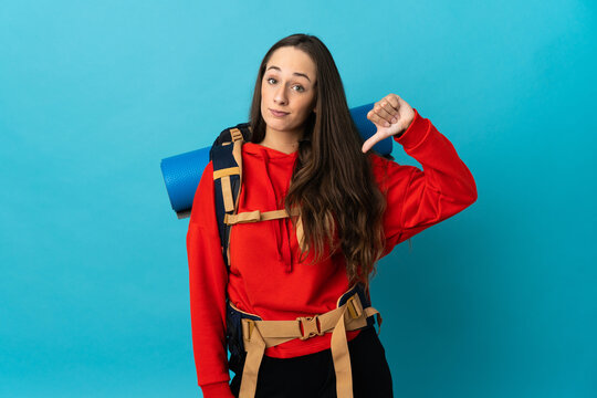Mountaineer woman with a big backpack over isolated background showing thumb down with negative expression