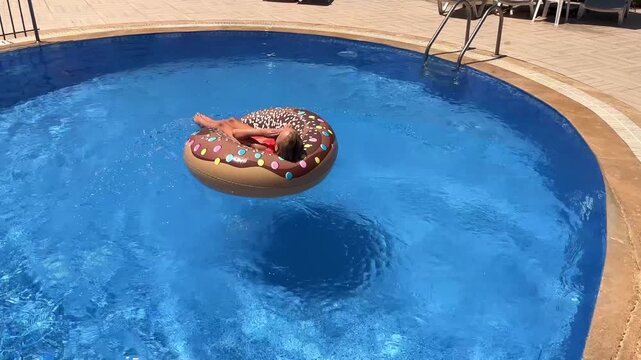 Slow motion video of a little girl jumping and landing on an inflatable donut swim ring in a blue swimming pool