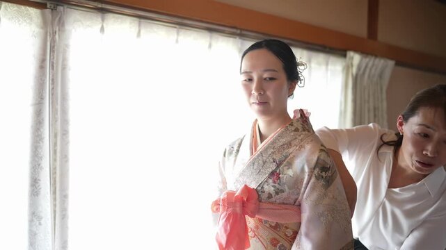 An assistant works behind a woman wearing a patterned kimono with a pink tie over the obi. Japan, April 19, 2025, spring.