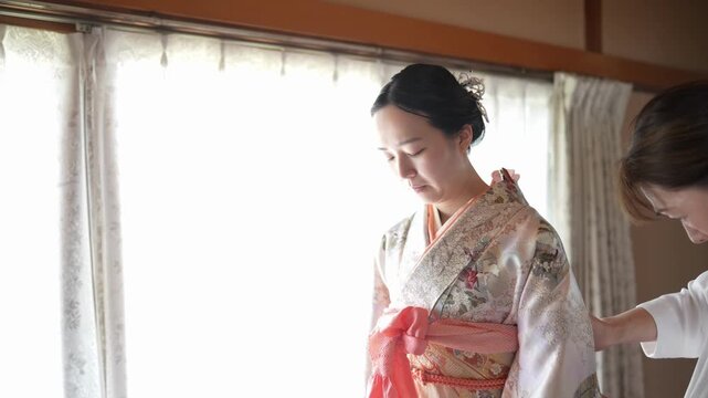 A woman looks down as an assistant adjusts her patterned kimono at the side of her waist. Japan, April 19, 2025, spring.