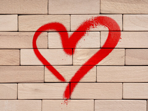 Red heart spray painted on wooden brick wall symbolizing love, romance and romantic relationship