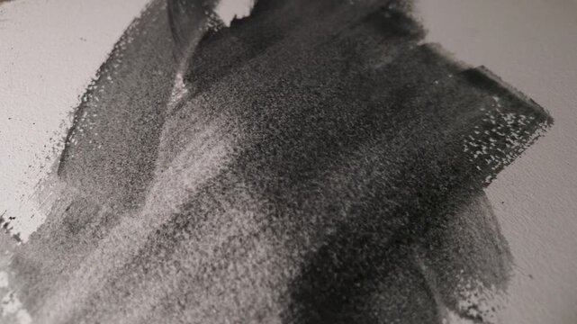 Watercolor graphite pigment forming granular brushstrokes on textured paper, irregular marks developing in slow motion