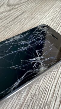 View of the broken phone screen. Cracked glass. A broken smartphone. Wooden background. Close up. 4k	