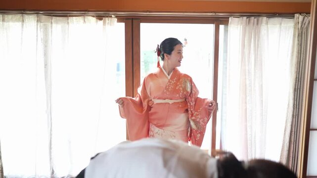 A woman looks down while holding out the sleeves of an orange floral kimono tied at the waist. Japan, April 19, 2025, spring.