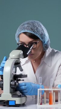 Female laboratory technician using a microscope for clinical analysis, working with test tubes for scientific discovery in a research facility dedicated to pharmaceutical advancements